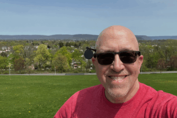 Dan Christ smiling outdoors in sunglasses and a red t-shirt, ready to help you master your personal tech.