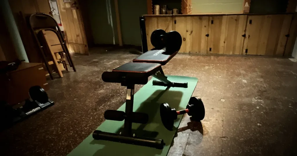 An empty weight bench and dumbbells sit unused on a mat in a dim basement, illustrating that owning a password manager is not the same as having a plan for it. Photo by Dan Christ.