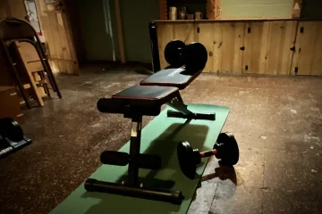 An empty weight bench and dumbbells sit unused on a mat in a dim basement, illustrating that owning a password manager is not the same as having a plan for it. Photo by Dan Christ.